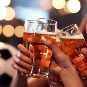 People clinking beer glasses cheering with a soccer ball in the background of the restaurant